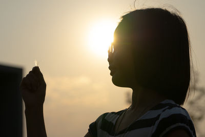 Closeup silhouette portrait of asian girl holds the grass flower in her hand with sunset background