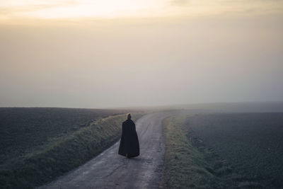 Woman with long coat walks in a path in a fog