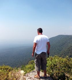 Rear view of man standing on mountain against clear sky