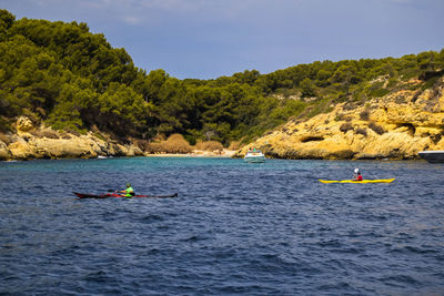 People kayaking in sea against sky