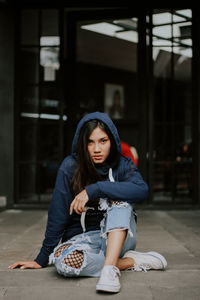 Portrait of young woman wearing hooded shirt sitting outdoors