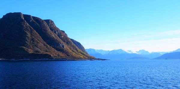 Scenic view of sea and mountains against clear blue sky