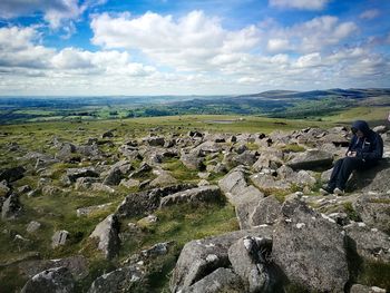 Rear view of people sitting on rock against sky