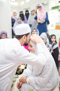 Groom kissing bride on forehead in wedding ceremony