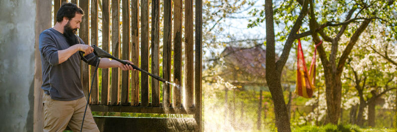 Man cleaning wooden railing in back yard