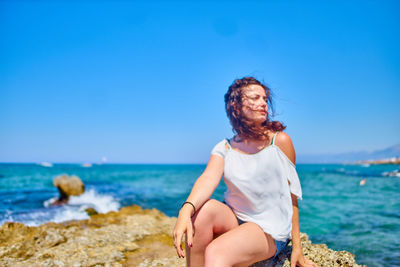 Young woman sitting on rock against sea at beach