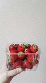 Close-up of hand holding strawberry over white background