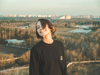 Portrait of smiling young woman standing on city against sky