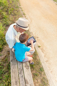 Grandson teaching digital tablet to grandfather while sitting in public park