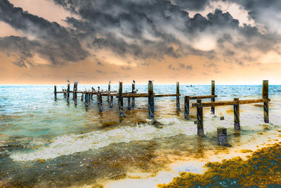 Wooden posts on beach against sky during sunset