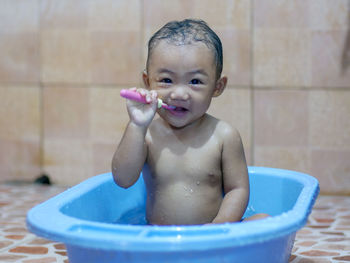 Portrait of cute shirtless baby boy with toothbrush sitting in bathtub 