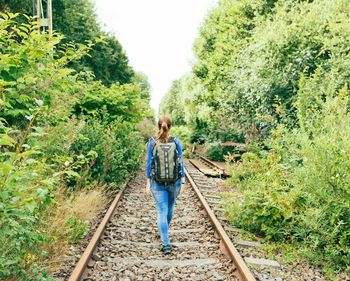 Rear view of woman walking on abandoned railroad track amidst plants