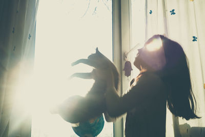 Side view of girl playing with by window at home