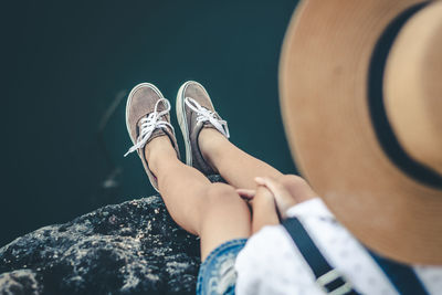 Low section of girl wearing hat sitting on rock over lake