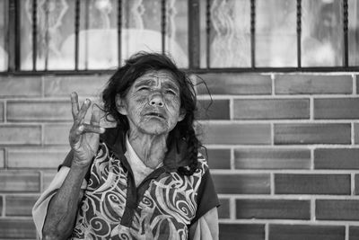 Senior woman gesturing against brick wall