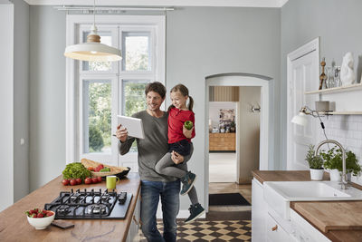 Happy father and daughter with bell pepper and tablet in kitchen