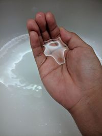 Cropped hand holding water over bathtub