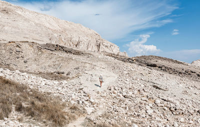 Rear view of tiny human walking on rocky path through arid terrain in summer.