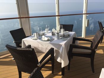 Chairs and tables in restaurant by sea seen through glass window