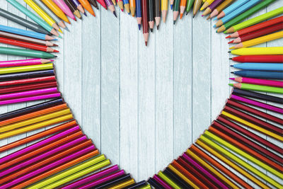 Directly above multi colored pencils forming heart shape on table