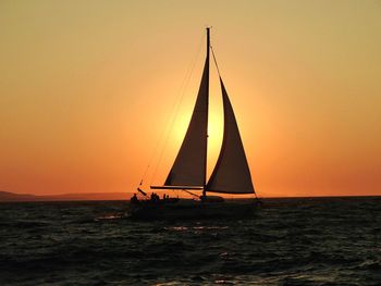 Silhouette sailboat sailing on sea against clear sky during sunset