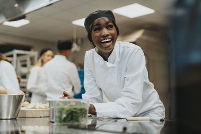 Cheerful female trainee leaning on kitchen counter