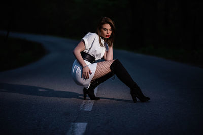 Portrait of young woman sitting on road in city