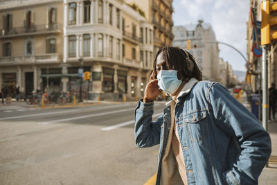 Young male hipster wearing protective face mask and listening music during covid-19