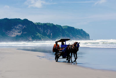 People riding motorcycle on beach against sky