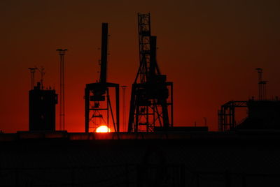 Low angle view of silhouette cranes against sky at sunset