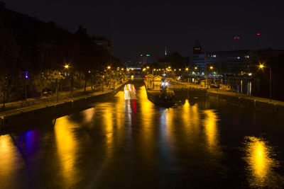 Illuminated buildings by river against sky at night