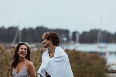 Smiling young man standing with woman by sea against sky