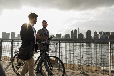 Usa, new york city, two businessmen with bicycle walking along east river