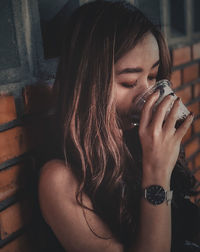 Beautiful young woman drinking coffee against wall