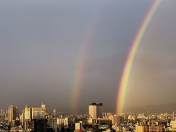 Rainbow over buildings in city against sky