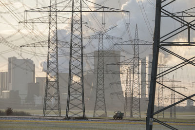 Germany, north rhine westphalia, niederaussem, tractor passing by electricity pylons and lignite power plant at sunset