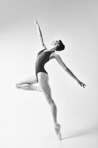 A ballerina in a bodysuit and pointesposes in a photo studio in motion showing beautiful long legs