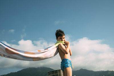 Boy on beach with towel flutters in wind like superman cape. happy child in summer against mountains