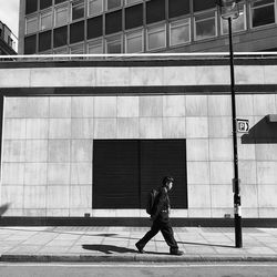 Side view of man walking on footpath against building