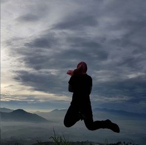 Woman standing on landscape against cloudy sky