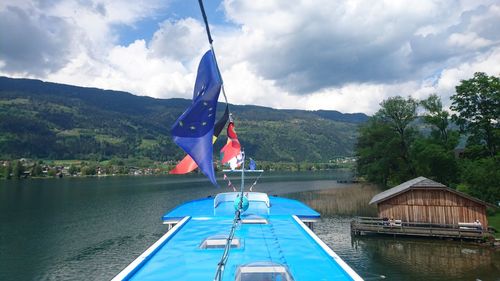 Flags on boat in lake against cloudy sky