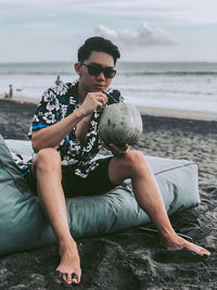 Full length of man drinking coconut water at beach