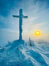 Cross on snowcapped mountain against sky during sunset