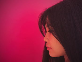 Side view of young woman against pink background