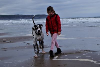 Girl walking with dalmatian dog at beach against cloudy sky