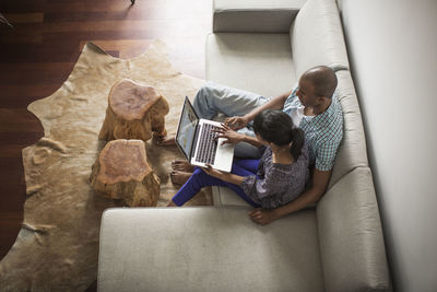 High angle view of couple using laptop computer while sitting on sofa at home