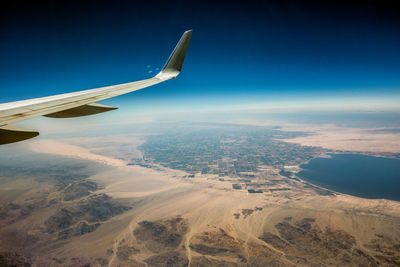 Aerial view of airplane flying over landscape against blue sky