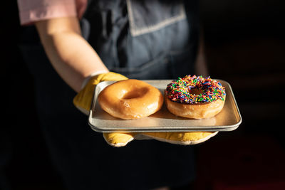 Midsection of person holding donut against black background