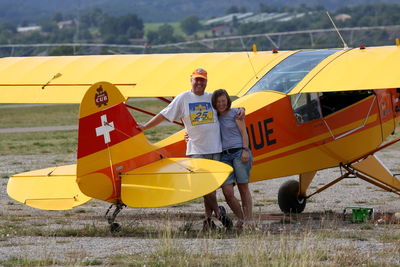 Smiling senior man standing with woman against yellow airplane