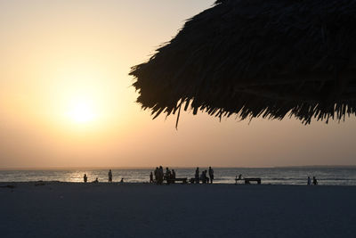 Silhouette people on beach against sky during sunset